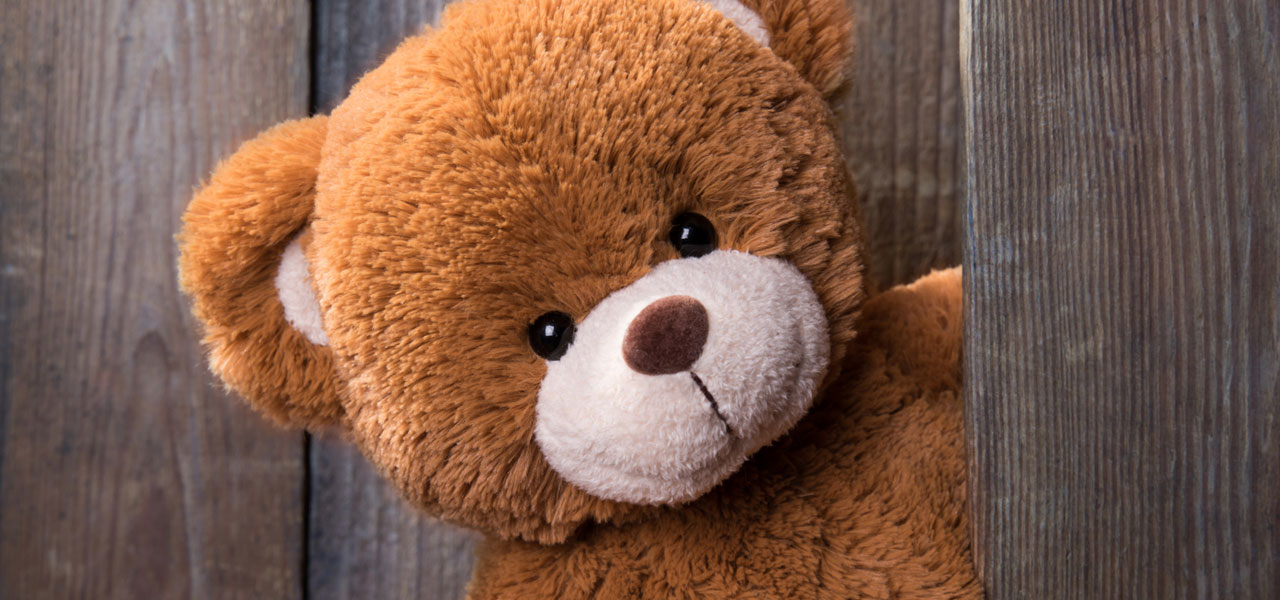 Ein Teddybär beugt sich aus einer geöffneten Tür und schaut den Betrachter frontal an