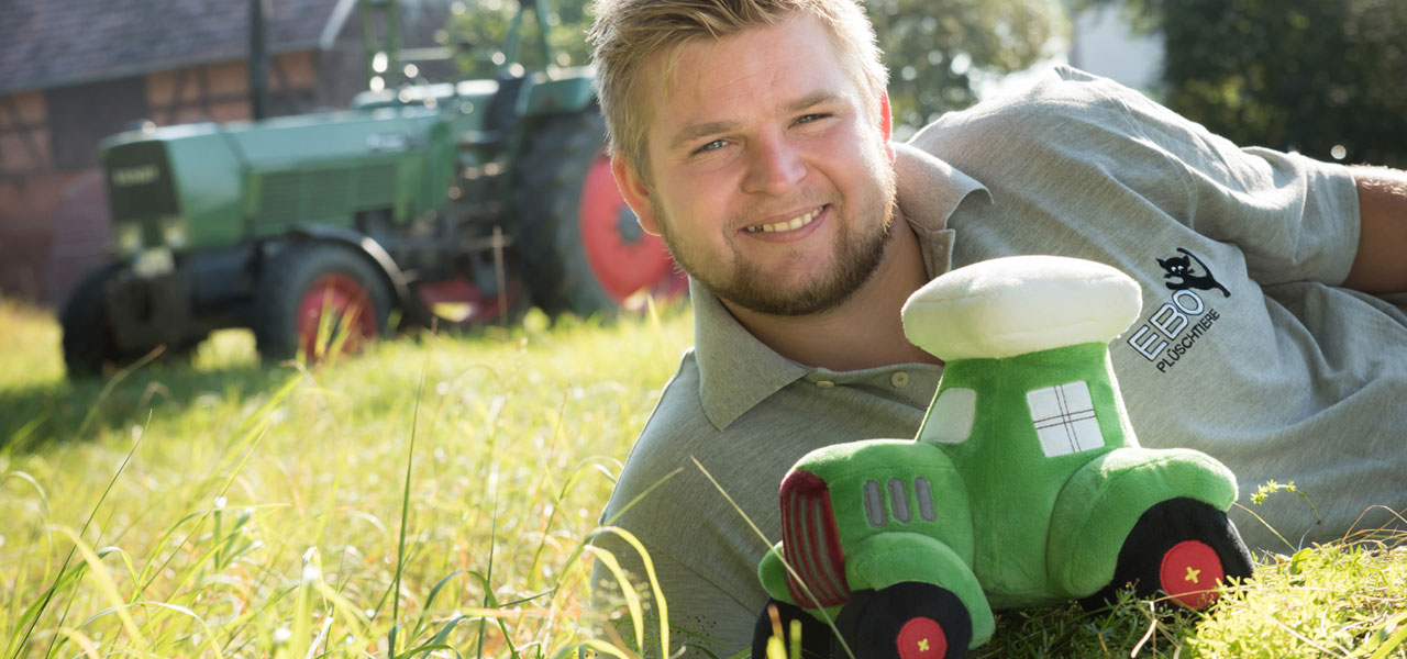 Mann mit Plüschtraktor und echtem Traktor im Hintergrund